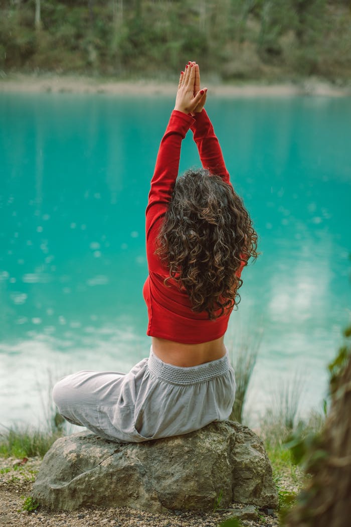 Back View of Woman Sitting on a Rock by a Body of Water and Meditating